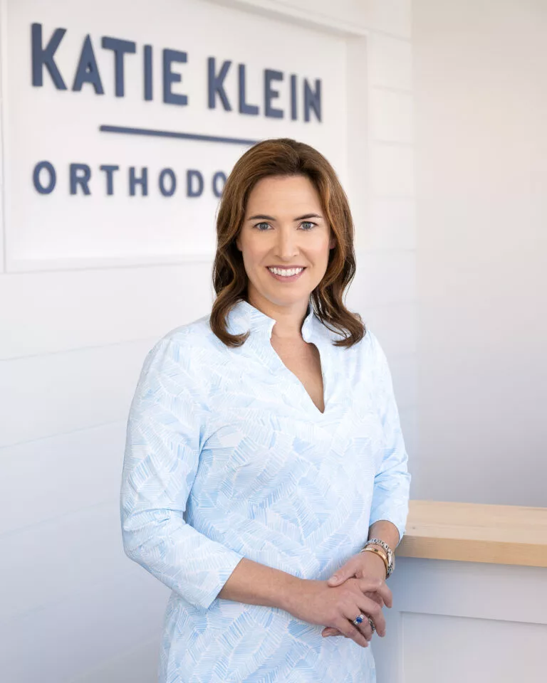 Portrait of Dr. Klein standing in the lobby in front of a Katie Klein Orthodontics sign